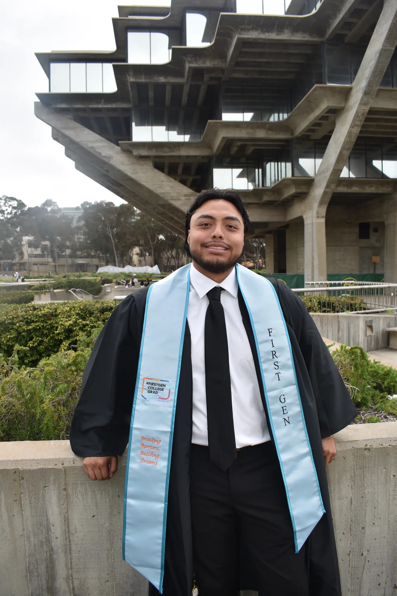 Alexander Lomeli in graduation regalia outside Geisel Library, UC San Diego